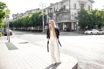 A beautiful girl with long even hair walks around the city, the model is wearing a black braid and white trousers