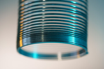 Closeup of coiled metal spring with sufficiently high strength and elastic properties in neon light. Macro photo, shallow depth of field.