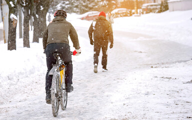 Man on bike cycling in snowy winter day, ride on snowy road in city. Biking in winter and cold weather, riding in cold conditions. Man in warm clothes wearing protective helmet riding on snowy road