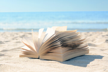 Fototapeta na wymiar Open book on sandy beach near sea