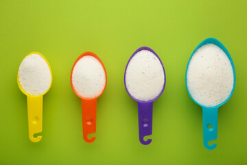 Measuring scoop with laundry powder on green background.