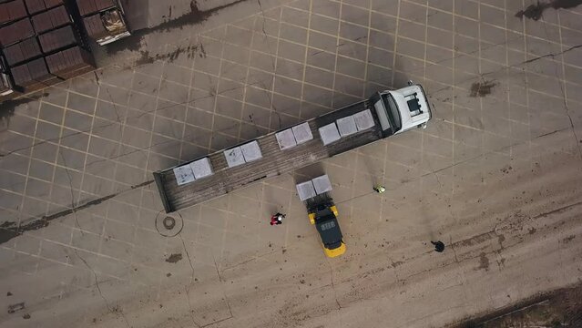 A loader car loads pallets with bricks onto a truck. Shooting from above