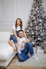 A man and his pregnant wife pose against the background of a Christmas tree