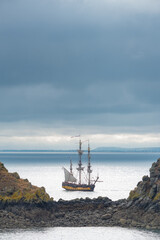 Sailing ship on the blue waters of the atlantic ocean on the coastline of Brittany, France, close to Cancale. Rocks at both sides. Dark clouds on the background. With copy-space.