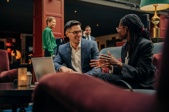 Smiling businessman looking at female colleague discussing while sitting in hotel lounge