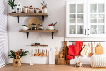The front view of part of a modern white kitchen and open shelves decorated for New Year in traditional colors. Eco items and homemade decorations.