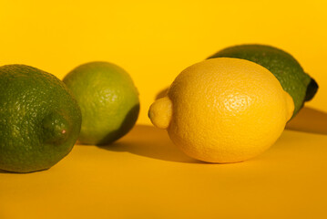 Yellow and green lemons fruit on yellow background with hard shadows. Citrus fruits. Green living and eco-friendly products