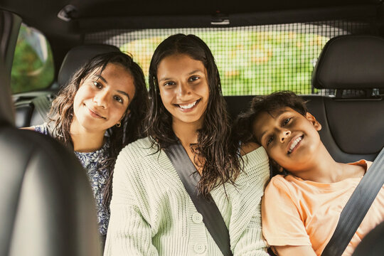Portrait of smiling siblings wearing seat belt while sitting together on back seat in car