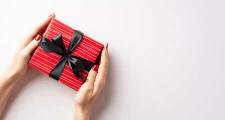 Black friday shopping concept. First person top view photo of young woman's hands giving red giftbox with black bow on isolated white background with copyspace