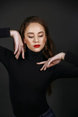 A model in bright make-up in a black sweater against the background of a dark wall