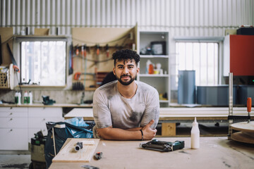 Portrait of smiling carpenter leaning on workbench