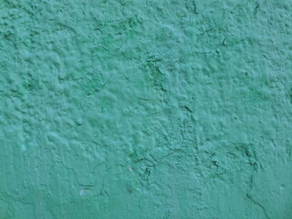 An old concrete wall with cracks and irregularities, covered with green paint.