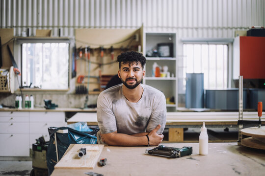 Portrait of smiling carpenter leaning on workbench