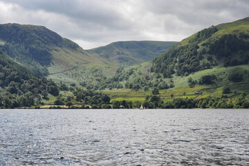 View from Ullswater looking towards the fells and mountains surrounding Glenridding with a yacht sailing by, Lake District, Cumbria, UK