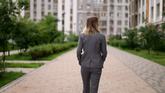 walk in city center, attractive slender lady in business suit is walking alone on street, rear view