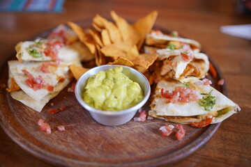 Chicken quesadilla with nachos and guacamole on a wooden plate.