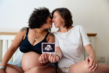 Happy couple kissing while showing an ultrasound scan picture of their baby. Lgbt couple and...