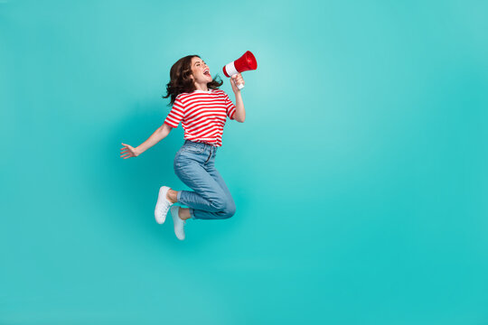 Full length photo of pretty cute girl dressed red t-shirt jumping high shouting bullhorn empty space isolated teal color background