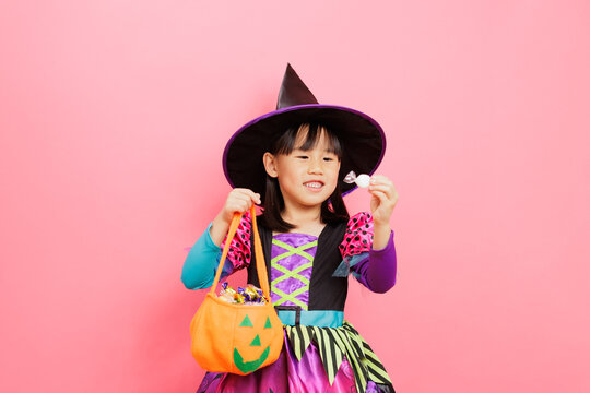 Happy Halloween! young girl with witch costume and hold a candy bucket against plain background
