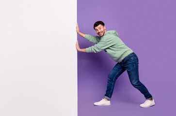 Full body photo of attractive young man pushing white banner wall cheerful wear trendy gray outfit...