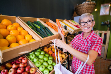 Mature woman buying goods in fruits and vegetables shop.