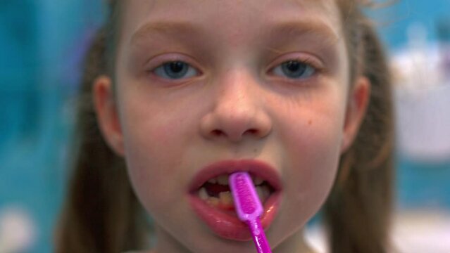 a little six-year-old girl brushes her teeth in the bathroom in front of a mirror, oral hygiene.