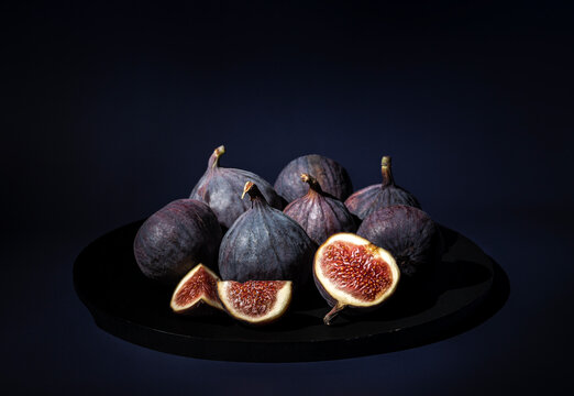 Blue figs and cut of fruit in a black plate on dark background. Heap of ripe figs for autumn vegan menu with natural vitamins.