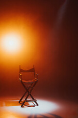 Fototapeta na wymiar The director's chair stands in a beam of light with an orange backlight and smoke. Place for text. Free chair. Concept of selection and casting. Shadow and light.