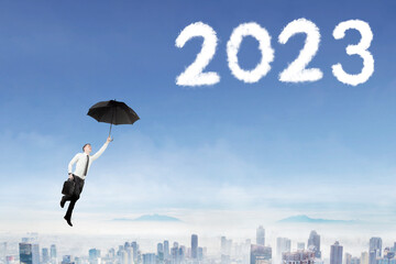 Businessman use umbrella to fly toward 2023 numbers