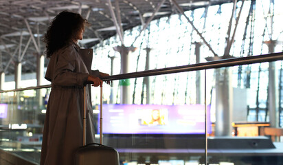 Fototapeta premium Airport. Beautiful woman with a suitcase at the airport is waiting for her departure. Migration and travel concept.