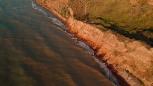 aerial footage of men running at early morning outdoor along sea shore under clay canyon on sea coast. active leisure and exercising at summer sunrise. healthy lifestyle and sport