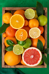 Different citrus fruits with leaves in a wooden box on a concrete background. Healthy food. Top view