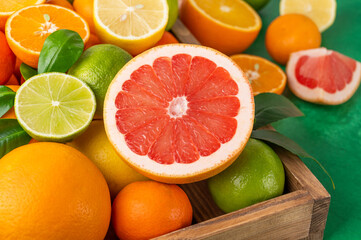 Different citrus fruits with leaves in a wooden box on a concrete background. Healthy food. Top view