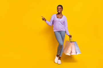 Full body portrait of pretty cheerful girl direct finger empty space hold packages isolated on yellow color background