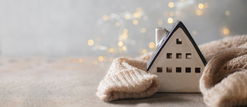 Ceramic house insulated by warm sweater. Concept of protection of house and lack of heat at home in winter. Banner image for design, web page