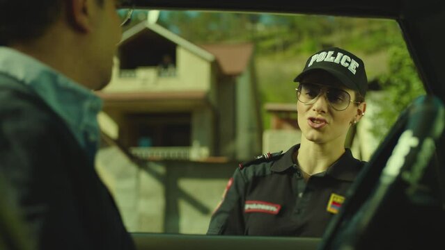 Beautiful woman in police uniform or female cop checking documents of man sitting in car on city street . Serious policeman checking male drivers license after exceeding speed limit . Giving honor .