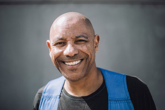 Portrait of happy bald construction worker against wall