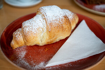 French butter croissant topped with powdered sugar, on a red plate next to a napkin
