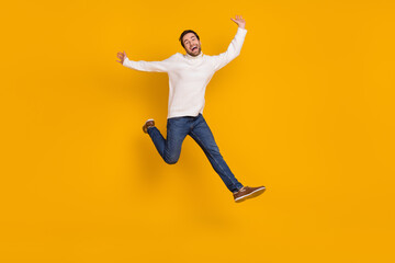 Fototapeta na wymiar Photo of funky childish guy dressed white sweater running jumping high isolated yellow color background