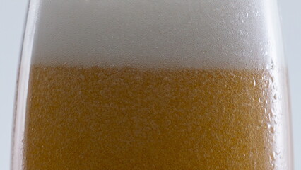 Beer white foam bubbling on glass at white background closeup. Bubbles swirling 