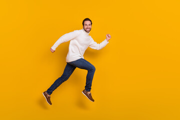 Fototapeta na wymiar Photo of pretty excited guy dressed white sweater running fast jumping high isolated yellow color background