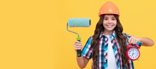 Builder teenager girl in helmet. happy child with curly hair in helmet hold paint roller and alarm clock, time. Child builder in helmet horizontal poster design. Banner header, copy space.