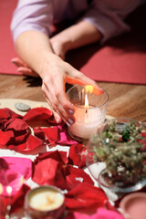 woman holding burning candle over flower petals, stones and dry herbs during spiritual session. magic ritual, spiritual energy mystic.