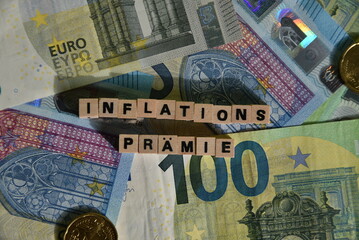 Das Wort Inflationsprämie mit Holzbuchstaben auf Euroscheinen