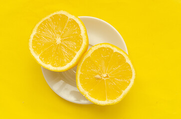 Top view, two slices of lemon on a white saucer on a yellow background