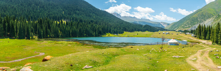 Panorama of Lake Alakol in Kyrgyzstan among tall clean fir trees