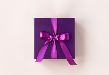 Violet gift box with a purple bow made of satin on soft beige background. St Valentines day, Birthday, New Year, Christmas, Mothers or Fathers day presents concept. 2023 Xmas symbol