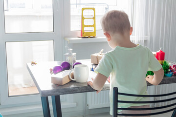 A small child with Christmas gifts is sitting at a New Year's wooden table with a tablet in his hands. Celebrating Christmas.