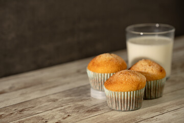 Glass of milk with three freshly baked muffins in the foreground - breakfast, snack, pastries concept