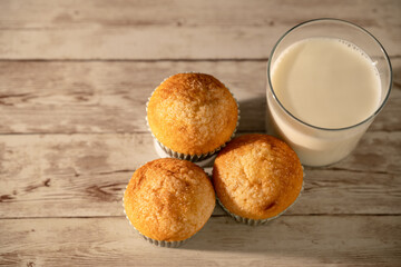 Glass of milk with three freshly baked muffins in the foreground - breakfast, snack, pastries concept